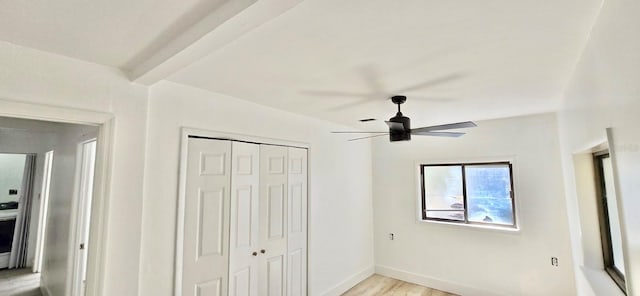 unfurnished bedroom featuring light wood finished floors, a closet, baseboards, ceiling fan, and beam ceiling