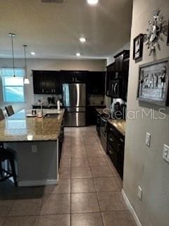 kitchen with tile patterned floors, a kitchen bar, a sink, freestanding refrigerator, and dark cabinets