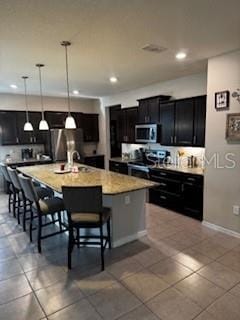 kitchen with decorative light fixtures, a kitchen bar, a large island, stainless steel appliances, and dark cabinets