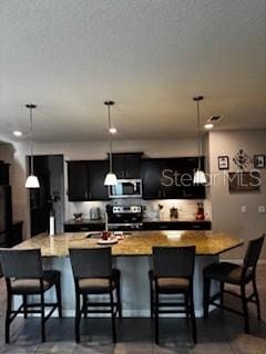 kitchen featuring a breakfast bar, a spacious island, dark cabinetry, stainless steel appliances, and hanging light fixtures