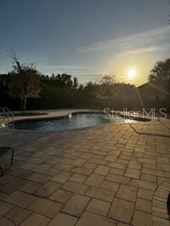 pool at dusk featuring a community pool and a patio area