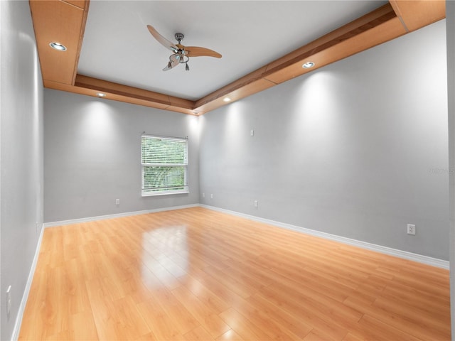 empty room featuring light wood-style flooring, recessed lighting, a ceiling fan, baseboards, and a raised ceiling