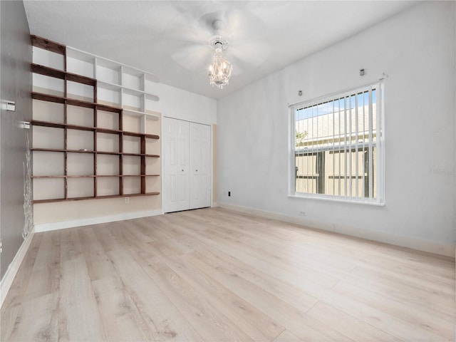 empty room with an inviting chandelier, baseboards, and wood finished floors