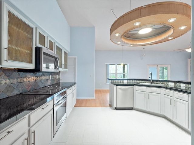 kitchen with dark countertops, glass insert cabinets, a sink, stainless steel appliances, and backsplash