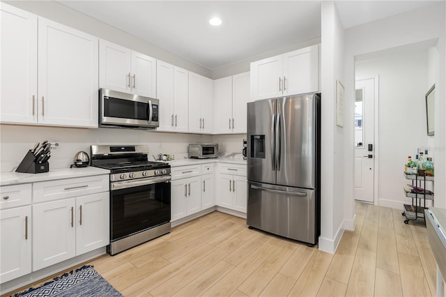 kitchen with light wood-type flooring, light countertops, appliances with stainless steel finishes, and white cabinets