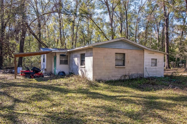 exterior space featuring a carport, concrete block siding, and a yard