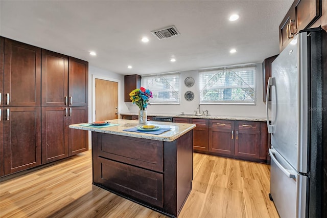 kitchen with visible vents, light wood-style flooring, freestanding refrigerator, a kitchen island, and a sink