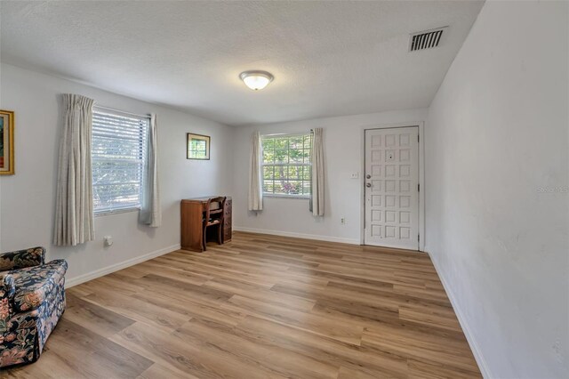 interior space featuring a textured ceiling, baseboards, visible vents, and light wood-style floors