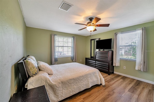 bedroom with baseboards, multiple windows, visible vents, and light wood-style floors