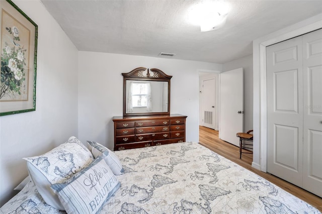 bedroom featuring a textured ceiling, a closet, wood finished floors, and visible vents