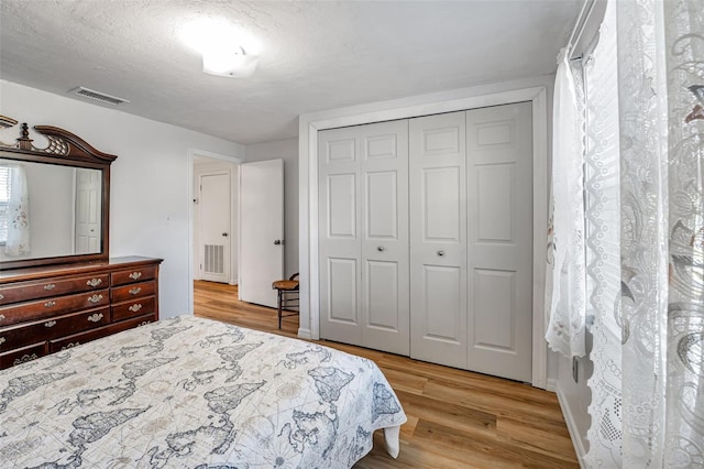 bedroom featuring baseboards, visible vents, light wood-style flooring, a textured ceiling, and a closet