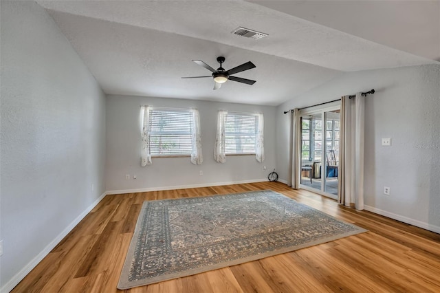 empty room featuring lofted ceiling, wood finished floors, visible vents, baseboards, and a ceiling fan