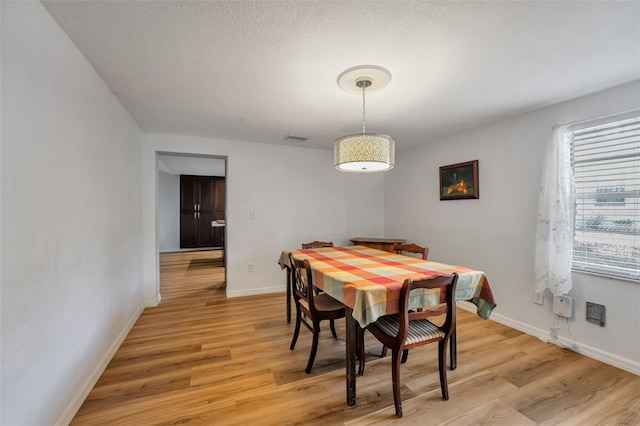 dining room featuring light wood-type flooring, visible vents, a textured ceiling, and baseboards