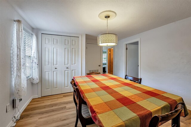 dining space featuring light wood-type flooring, visible vents, a textured ceiling, and baseboards