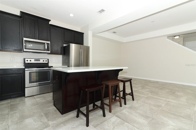 kitchen featuring stainless steel appliances, light countertops, visible vents, a kitchen island, and dark cabinets