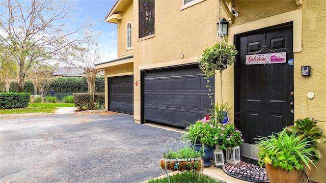 property entrance with an attached garage, driveway, fence, and stucco siding