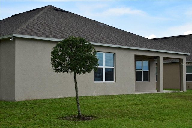 view of side of property with a shingled roof, a yard, and stucco siding