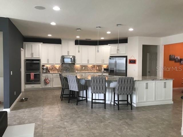 kitchen with stainless steel appliances, tasteful backsplash, a large island with sink, and white cabinetry