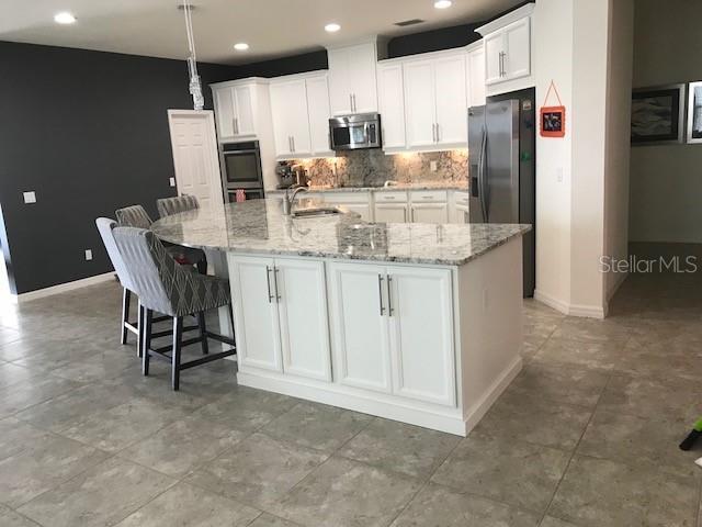 kitchen featuring stainless steel appliances, a sink, white cabinetry, a large island, and tasteful backsplash