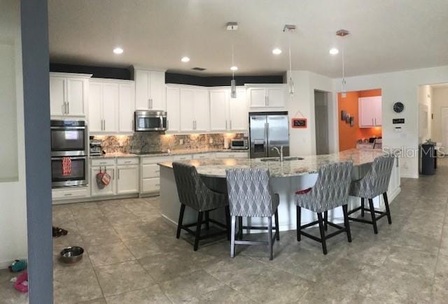 kitchen featuring tasteful backsplash, white cabinets, appliances with stainless steel finishes, a kitchen breakfast bar, and a large island with sink