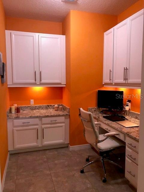 office space featuring a textured ceiling, built in desk, tile patterned floors, and baseboards