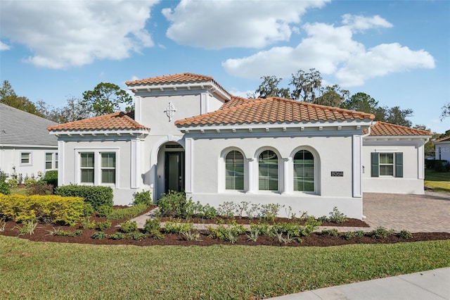 mediterranean / spanish home with a tile roof, a front yard, and stucco siding