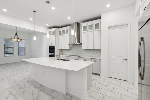 kitchen with appliances with stainless steel finishes, a sink, marble finish floor, wall chimney range hood, and backsplash