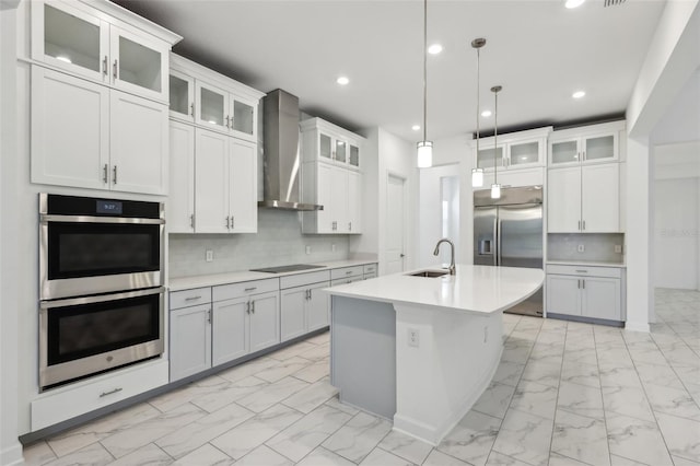 kitchen featuring stainless steel appliances, a sink, marble finish floor, wall chimney range hood, and decorative backsplash