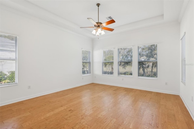 spare room with a tray ceiling, a healthy amount of sunlight, visible vents, and light wood-style flooring