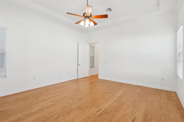 spare room featuring a tray ceiling, visible vents, light wood-style floors, ornamental molding, and baseboards