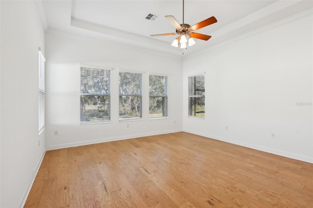 spare room featuring light wood-style floors, baseboards, visible vents, and a tray ceiling