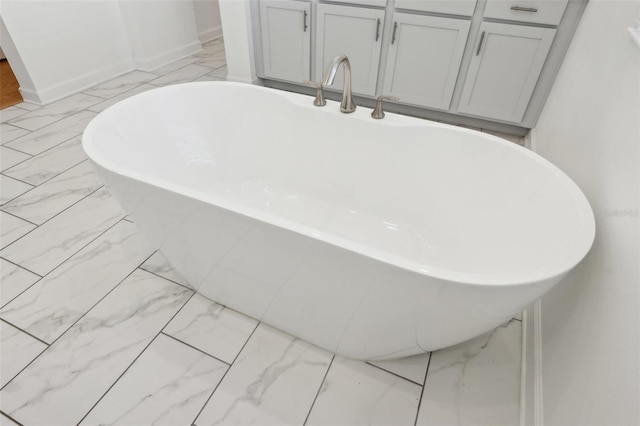 full bathroom with marble finish floor, a freestanding bath, and baseboards