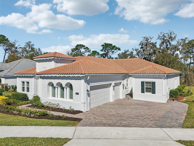 mediterranean / spanish-style house featuring a garage, decorative driveway, a tiled roof, and stucco siding