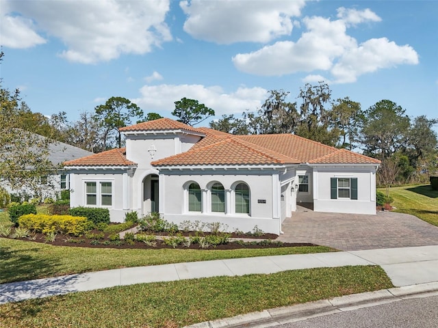 mediterranean / spanish house featuring a tiled roof, a front lawn, driveway, and stucco siding