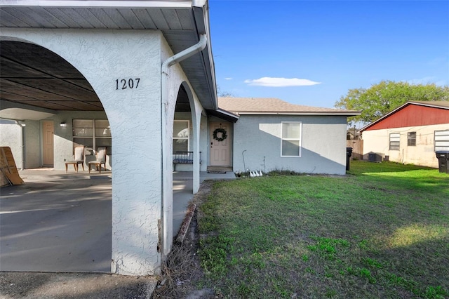 exterior space featuring a yard, roof with shingles, cooling unit, and stucco siding