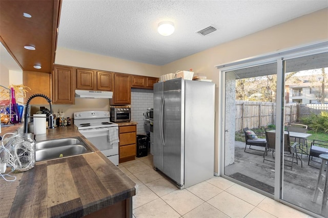 kitchen featuring light tile patterned flooring, under cabinet range hood, electric stove, freestanding refrigerator, and dark countertops