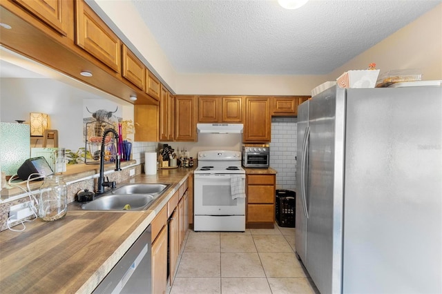 kitchen with light tile patterned floors, stainless steel appliances, brown cabinetry, a sink, and under cabinet range hood