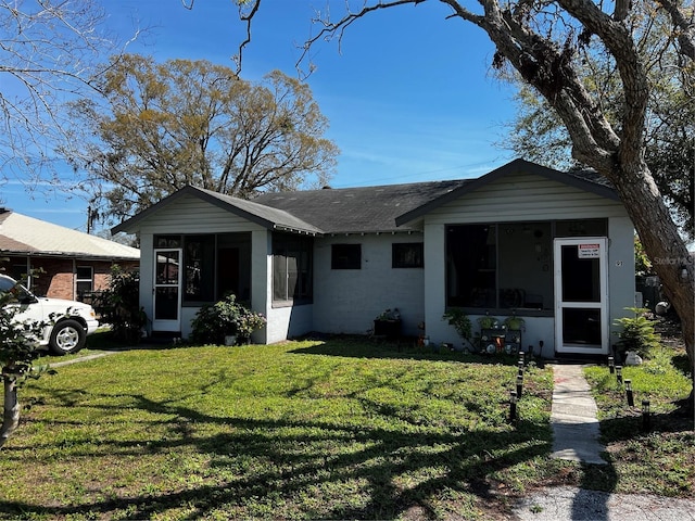 view of front facade with a sunroom, a shingled roof, concrete block siding, and a front yard