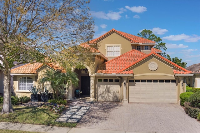 mediterranean / spanish-style house with a garage, a tiled roof, decorative driveway, and stucco siding