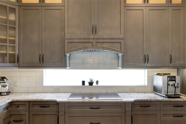 kitchen featuring tasteful backsplash, light stone countertops, glass insert cabinets, and black electric cooktop