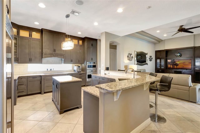 kitchen with open floor plan, light tile patterned floors, visible vents, and a large island with sink