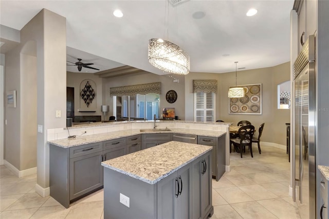 kitchen with light stone counters, a center island, stainless steel appliances, gray cabinets, and a sink