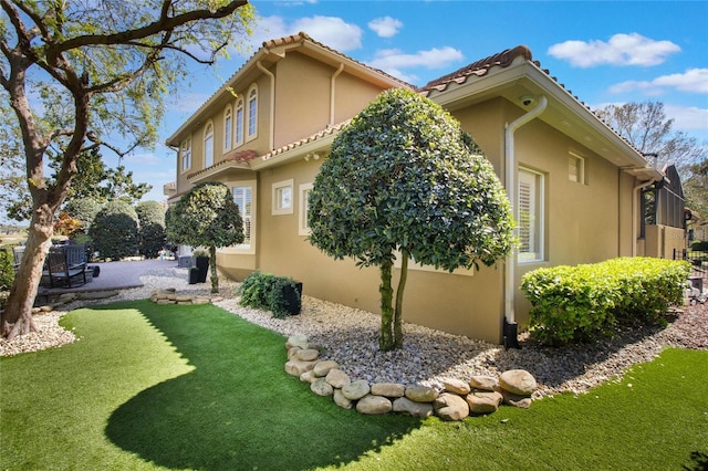 view of property exterior featuring a yard, a tile roof, and stucco siding