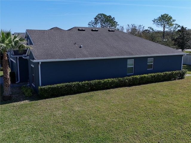 view of side of property with a shingled roof and a lawn