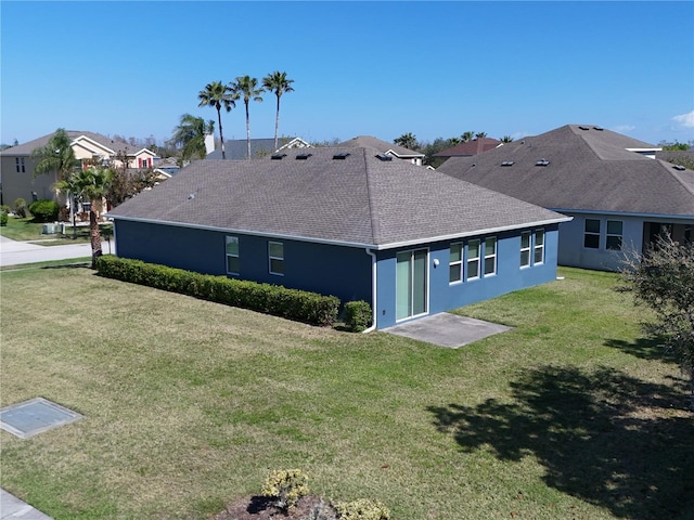 rear view of house featuring a yard, roof with shingles, a residential view, and stucco siding