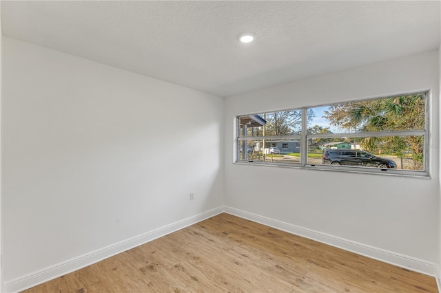 spare room featuring light wood finished floors, baseboards, and a textured ceiling