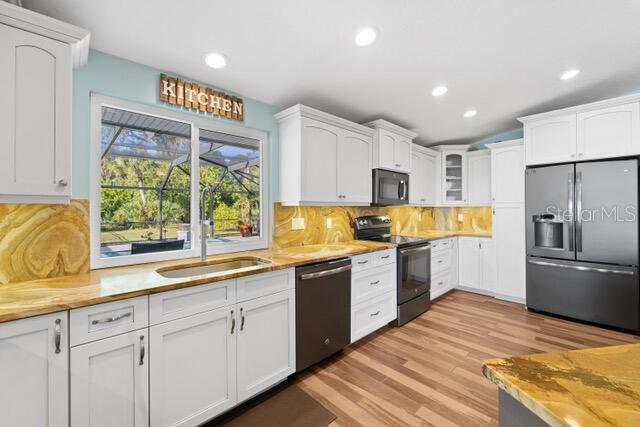 kitchen featuring white cabinetry, appliances with stainless steel finishes, backsplash, light wood finished floors, and glass insert cabinets