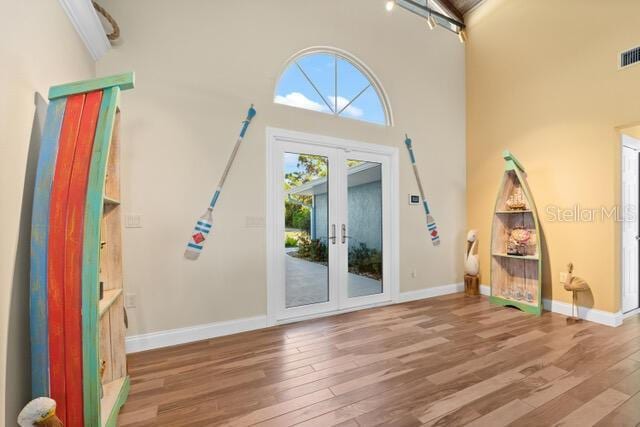 interior space featuring baseboards, visible vents, wood finished floors, a high ceiling, and french doors