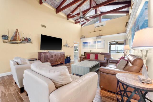 living area featuring baseboards, visible vents, wood finished floors, beamed ceiling, and high vaulted ceiling