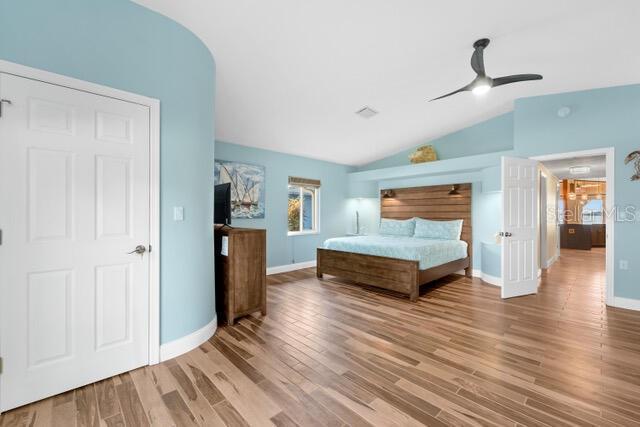 unfurnished bedroom featuring lofted ceiling, arched walkways, wood finished floors, a ceiling fan, and baseboards